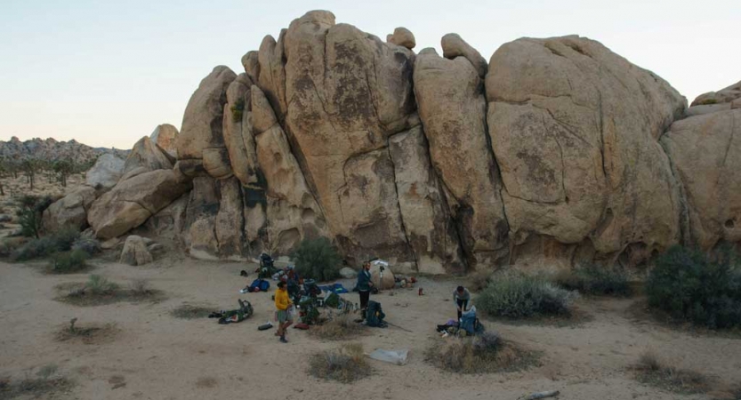 A group of people appear small beside a large rock formation. 